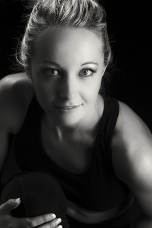 Beautiful fit and healthy blond woman portrait in a black top with knee drawn up artistic conversionの写真素材