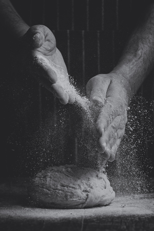 Flour is sprinkled over a ball of dough on wooden board by hand in artistic conversionの写真素材