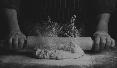 Man with apron rolling a ball of dough on a wooden board by hand in artistic conversion