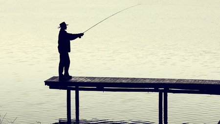 Man with fly-fishing gear catching a trout from a jetty on a foggy morningの写真素材