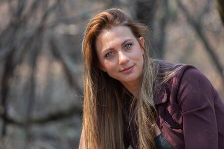 Portrait of a brunet woman with a blue denim and maroon jacket sitting big rocksの写真素材