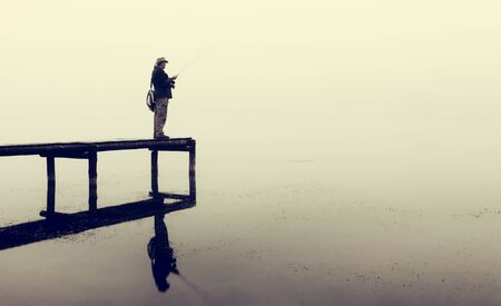 Man with fly-fishing gear catching a trout from a jetty on a foggy morningの写真素材