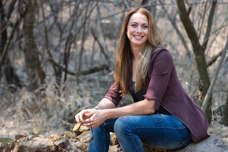Portrait of a brunet woman with a blue denim and maroon jacket sitting big rocksの写真素材