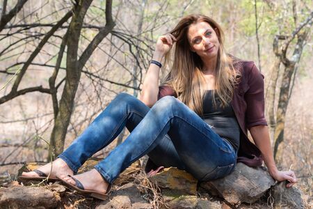 Portrait of a brunet woman with a blue denim and maroon jacket sitting big rocksの写真素材