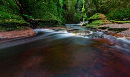 Small river with red water flowing through Finnich Glen landscape photographyの写真素材
