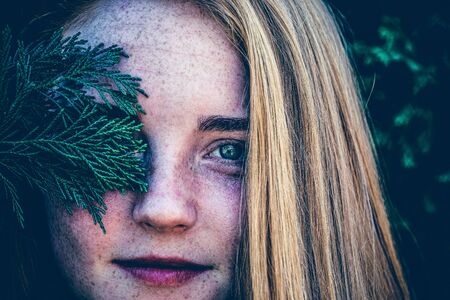 Portrait of a redhead woman with green pine leaves in the background in artistic conversionの写真素材