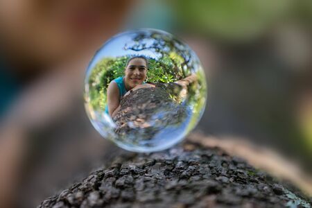 Portrait of a woman in a lensball on a tree trunk with rough barkの写真素材