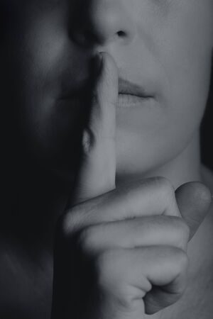Conceptual monochrome image of woman holding finger to her lips to keep quietの写真素材