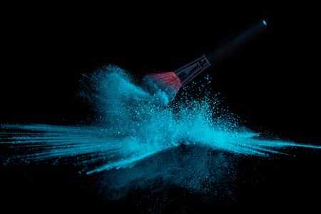 Blue makeup powder brush fall on a shiny black surface in a dust cloudの写真素材