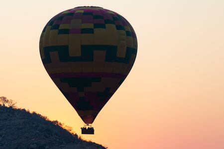 One hot air balloon floating over low hills into an orange sunsetの写真素材