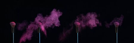Four make-up brushes with sequence of pink powder explosions on a black backgroundの写真素材