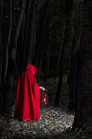 Attractive woman dressed a little red riding-hood walk in a dark forest with a lanternの写真素材