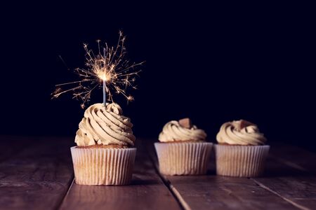 Three cupcakes on a table with a sparkle and a black backgroundの写真素材