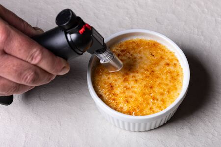 Chef making a crÃ¨me brulee in a small white bowl with a torch flameの写真素材