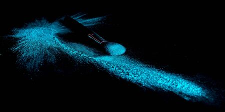 Blue makeup powder brush fall on a shiny black surface in a dust cloudの写真素材