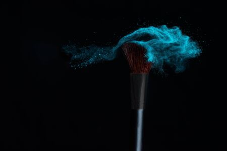 Make-up brush with blue powder explosion isolated in a black backgroundの写真素材