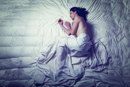 Conceptual image of a woman a sad and lone on a bed under a sheetの写真素材