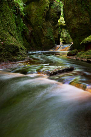 Small river with red water flowing through Finnich Glen landscape photographyの写真素材