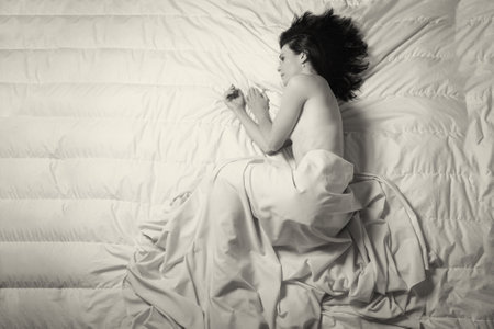 Conceptual image of a woman a sad and lone on a bed under a sheetの写真素材