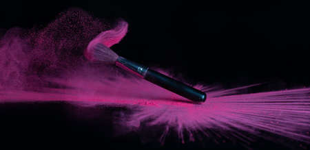 Pink makeup powder brush fall on a shiny black surface in a dust cloudの写真素材