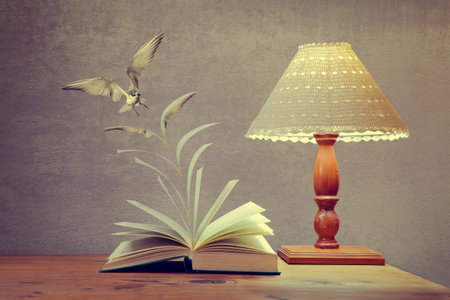 Artistic conversion of an open book on table with pages to become a flying bird in colour with shining bed lampの写真素材