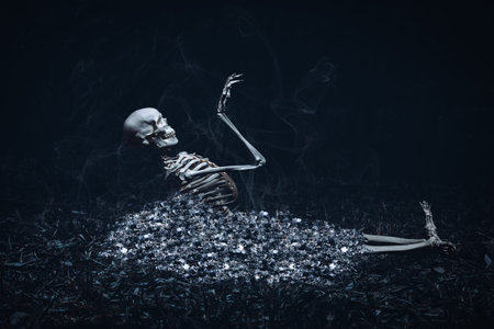Conceptual image of a skeleton emerging from a bed of glowing ashes, surrounded by smoke in a dark,...