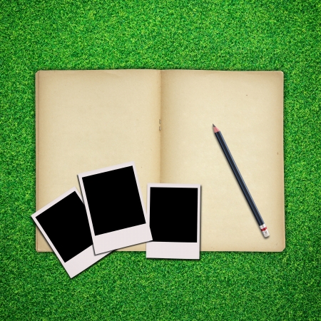 Pencil and photo frame with old book on green grass backgroundの写真素材