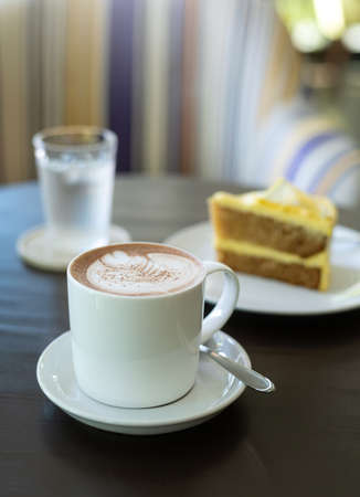 cup of hot coffee art with cake on wooden table in cafeの写真素材