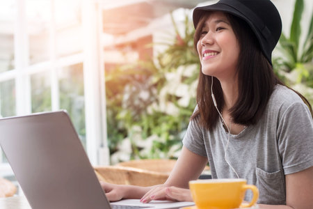 young hipster woman using laptop and listening music with earphone in coffee shop backgroundの写真素材