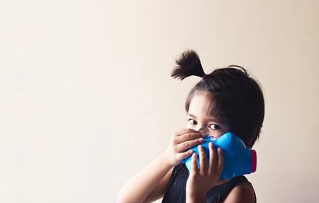 Asian kid and coin in hand putting on blue piggy bank, vintage color style, soft focus and blur, blank textの写真素材