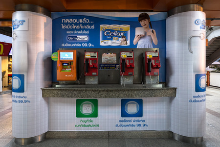 public payphone and top up machine on the corner with advertisement poster in Thai language in the background at BTS Mo Chit station in the eveningのeditorial素材