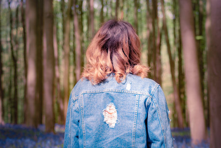 Back view of a young girl wearing denim jacket and the sun lighting up the curls in her hair,...
