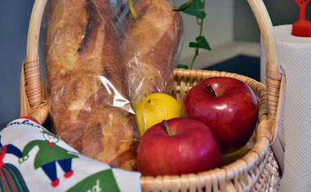 Apples, lemon and breads in a basket on a tableの写真素材