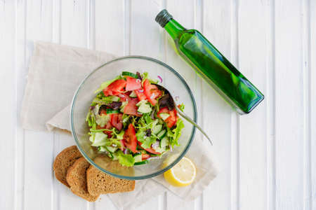taste of vegetarian summer concept, salad of lettuce leaf, tomato, cucumber, onion, oregano with olive oil and lemon juice on white wooden background with copyspaceの写真素材