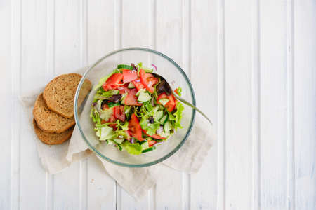 taste of vegetarian summer concept, salad of lettuce leaf, tomato, cucumber, onion, oregano with olive oil and lemon juice on white wooden background with copyspaceの写真素材