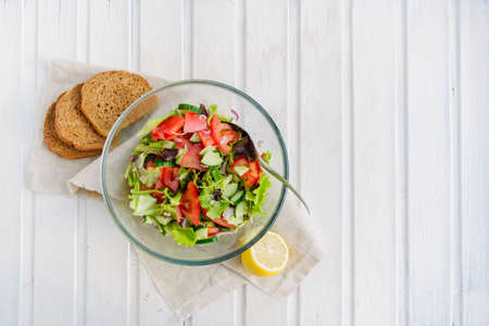 taste of vegetarian summer concept, salad of lettuce leaf, tomato, cucumber, onion, oregano with olive oil and lemon juice on white wooden background with copyspaceの写真素材
