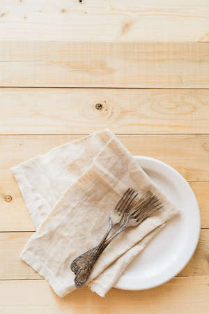 Top view wooden table setting with copyspace, three antique forks and linen napkin on white plateの写真素材