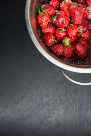 strawberries in a colander on a black desktop backgroundの写真素材