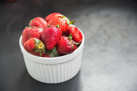 strawberries in white bowl on black slate backgroundの写真素材