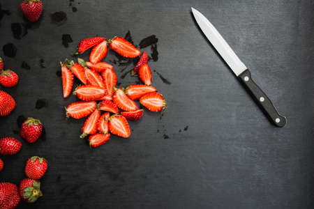 whole and sliced strawberries and knife on black background with copyspaceの写真素材