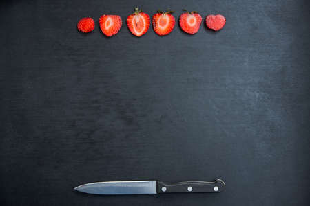 sliced strawberries and knife on black background with copyspaceの写真素材