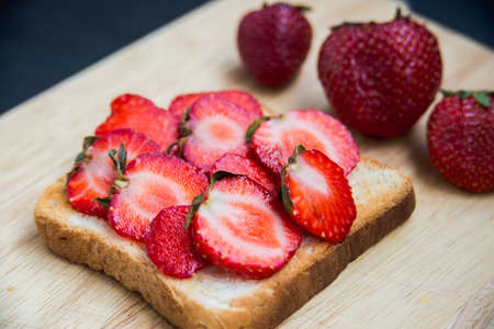 Toast with cheese and strawberries on cutting boardの写真素材