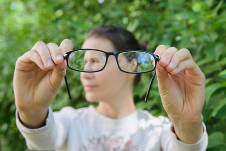 thinking young woman holding glasses on background of green plantsの写真素材
