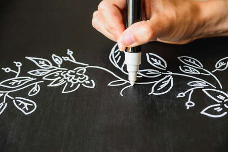 woman draws chalk marker autumn pattern on a black boardの写真素材
