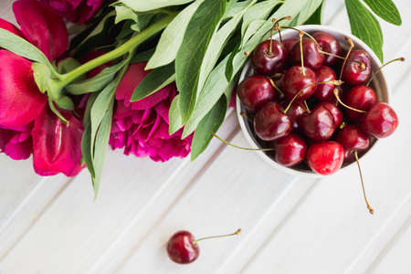 cherries in bowl with bouquet peonies on white backgroundの写真素材