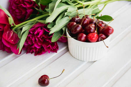 cherries in bowl with bouquet peonies on white backgroundの写真素材
