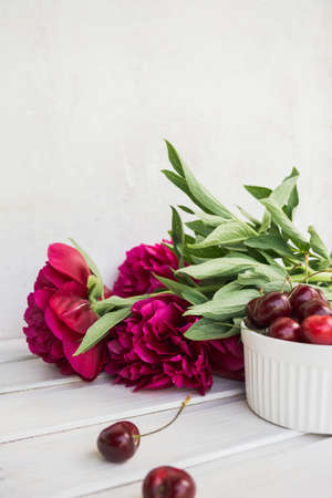 cherries in bowl with bouquet peonies on white backgroundの写真素材