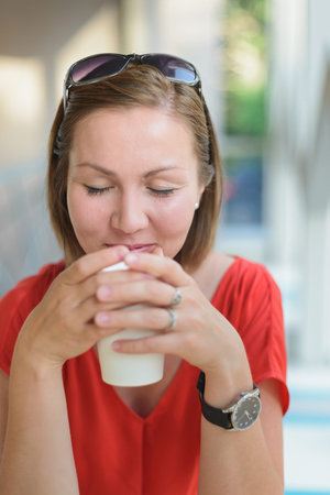 young woman in red dress drinking drink at cafe near window