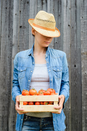 young woman holds box with crop of tomatoes