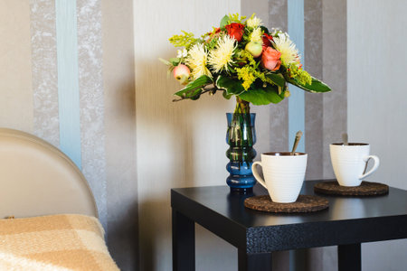 two cups of hot drink near bouquet of flowers in vase on table in apartmentの写真素材